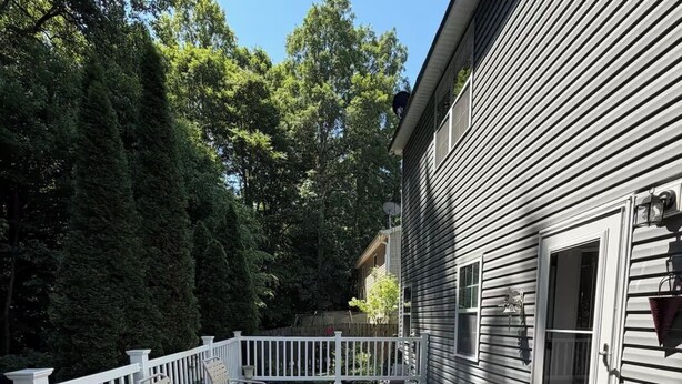 Um deck de madeira com guarda-corpos brancos, uma área de varanda coberta e uma casa com janela e porta.