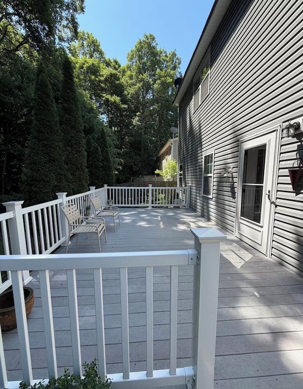 A wooden deck with white railings, a covered patio area, and a house with a window and door.