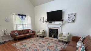 Uma sala de estar com piso de madeira, lareira, televisão de tela plana e dois sofás.