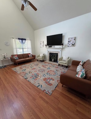 A living room with hardwood flooring, a fireplace, a flat-screen TV, and two sofas.