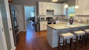 Uma cozinha moderna com armários brancos, uma ilha central com banquetas, eletrodomésticos de aço inoxidável e iluminação pendente.
