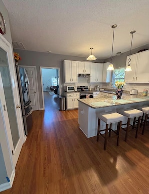 A modern kitchen with white cabinets, a central island with bar stools, stainless steel appliances, and pendant lighting.