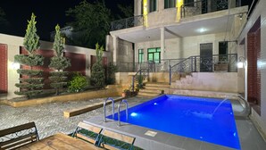 A pool with a wooden deck and a table, surrounded by potted plants and a building with a balcony. - Spacious 7-bedroom house in peaceful Baku with AC (Baku)