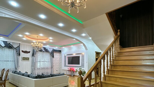 A spacious living area with a wooden staircase, a chandelier, and a flat-screen TV. - Spacious 7-bedroom house in peaceful Baku with AC (Baku)