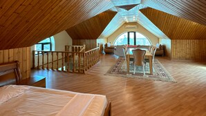 A high-ceilinged attic bedroom with a wooden floor, a bed, a dining area with a table and chairs, and a view through a large window. - Spacious 7-bedroom house in peaceful Baku with AC (Baku)
