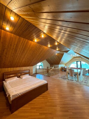 A spacious attic bedroom with a large bed, wooden ceiling, and a view through a skylight.