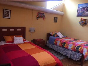 Ein Zimmer mit zwei Betten, einer Wandlampe, einem kleinen Tisch und einem Bild.