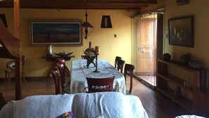 Un comedor con una mesa dispuesta para cuatro personas, sillas de madera, una araña y un cuadro en la pared.
