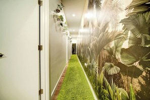 Ein Flur mit einem grünen Kunstgrase-Boden, weißen Wänden und einem Wandbild mit tropischer Vegetation.