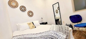 Ein Schlafzimmer mit einem Bett, einem Spiegel, einem blauen Stuhl und Wanddekorationen.