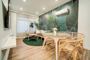 A modern living room with a round glass table, wicker chairs, a sofa, and a large green patterned wall. - The Urban Garden • Luxury 3BR Oasis Near Fishtown (Philadelphia)