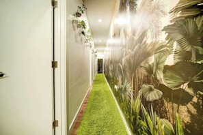 A hallway with a green artificial grass floor, a wall with a tropical plant mural, and a door on the left. - The Urban Garden • Luxury 3BR Oasis Near Fishtown (Philadelphia)