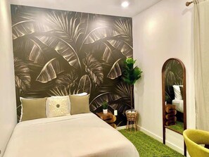 A bedroom with a bed, a mirror, a plant, and a wall with a leaf pattern. - The Urban Garden • Luxury 3BR Oasis Near Fishtown (Philadelphia)