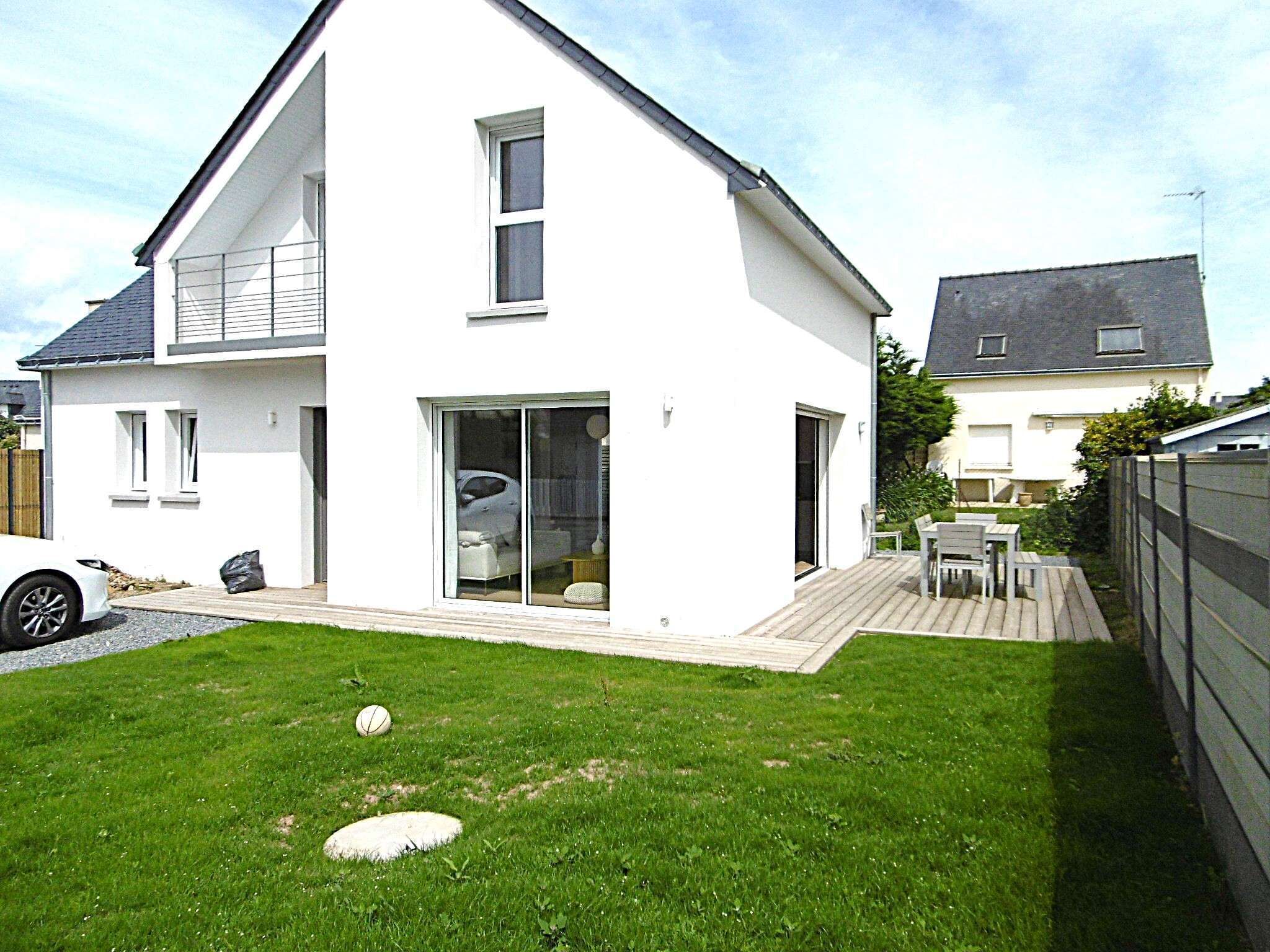A modern two-story house with a large glass sliding door, a wooden deck, and a well-maintained lawn.