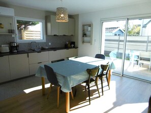 A modern kitchen with a dining area, featuring a table with chairs, a hanging light fixture, and a view through a glass door. - House 4 rooms 6 to 8 people near the sea (SARZEAU)