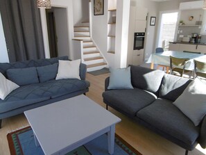 A modern living room with a sofa, a coffee table, and a staircase leading to a kitchen area. - House 4 rooms 6 to 8 people near the sea (SARZEAU)