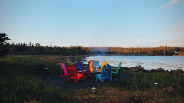 A lakeside setting with a fire and colorful Adirondack chairs.