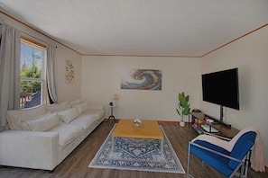 A living room with a sofa, a coffee table, a TV, a plant, and artwork on the walls.