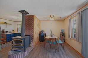 A cozy living room with a fireplace, a dining area with a table and chairs, and a kitchen area with blue cabinets and a brick wall.