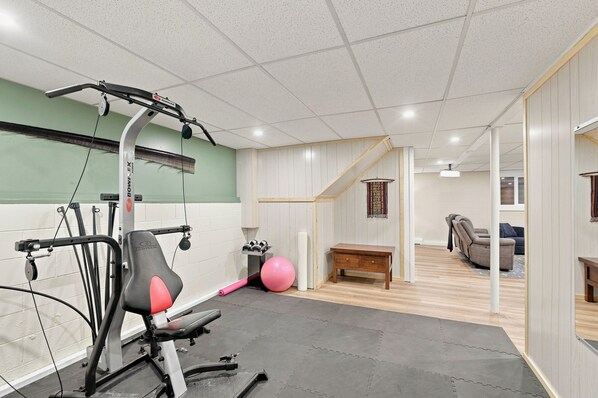 A gym with exercise equipment, a yoga mat, and a staircase leading to a living area.