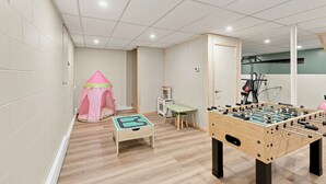 A room with a foosball table, a play area with a pink tent, and a small table with a toy kitchen set.