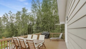A wooden deck with a table and chairs, a grill, and a covered barbecue area.