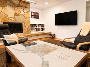 Olohuone, jossa on kiviseinä, takka, kirjahyllyt, litteänäyttöinen televisio ja sohvapöytä, jonka päällä on kartta.