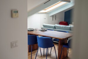 Et spiseområde med et træbord og blå stole, en lyseblå sofa og en rød pude i baggrunden.