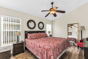 A bedroom with a bed, a ceiling fan, a nightstand, a lamp, a mirror, and a window with blinds. - Disney World Retreat Oasis & Private Pool (Kissimmee)