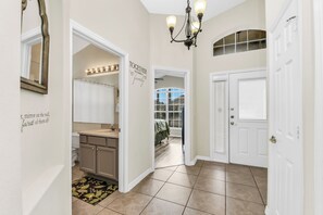 A hallway with a mirror, a chandelier, a sign that says 'TOGETHER we make a family,' and a view into a bedroom. - Disney World Retreat Oasis & Private Pool (Kissimmee)