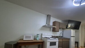 A compact kitchen with a microwave, stove, sink, and a television mounted on the wall.