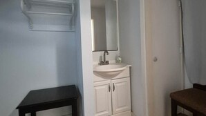 A room with a wooden floor, a white sink with a mirror above it, a black table, and a door with a curtain.