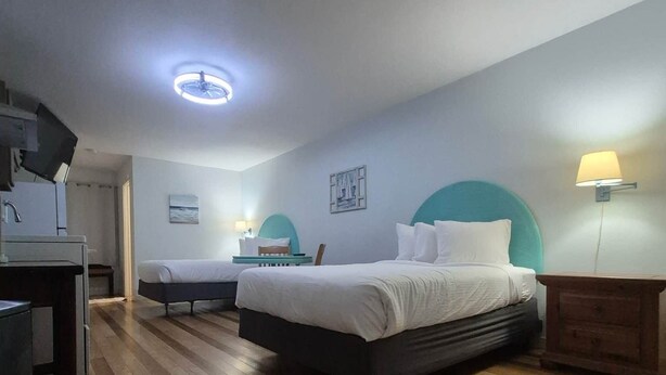 A hotel room with a bed, bedside table, lamp, and a desk with a chair.