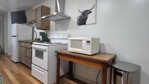 Una cocina con electrodomésticos blancos, una mesa de madera y un bote de basura.
