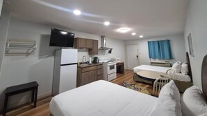 Una habitación compacta con cama, kitchenette, televisión y una puerta que da a otra habitación.