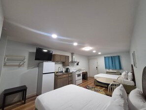 A compact room with a bed, a kitchenette, a television, and a door leading to another room.