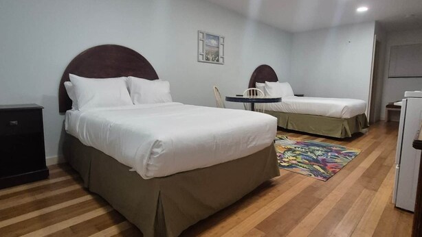 Habitación de hotel con dos camas, una mesita, una silla, un tapete colorido y un refrigerador.