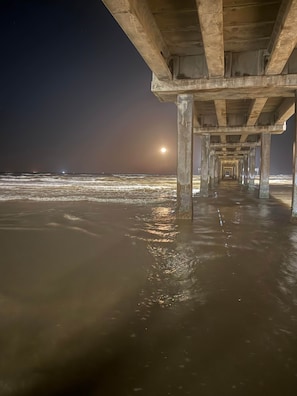 Une jetée constituée de piliers en béton, offrant une vue sur l’océan la nuit.