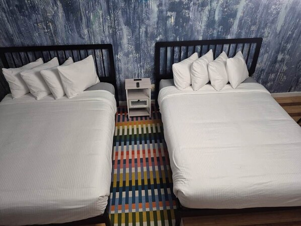 A room with two beds, a small nightstand, and a colorful striped rug.