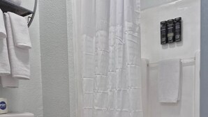 Un baño con inodoro, ducha con cortina blanca y toallero con toallas.