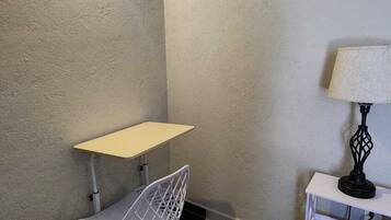 Una habitación pequeña con piso a cuadros, una silla blanca, una mesita y una lámpara sobre una mesita auxiliar.