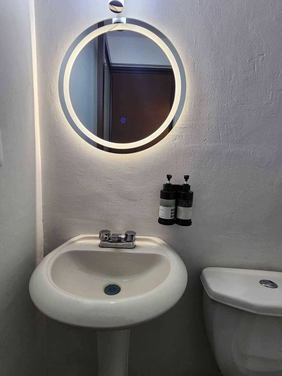 A bathroom with a white sink, a toilet, and a mirror with a circular light.