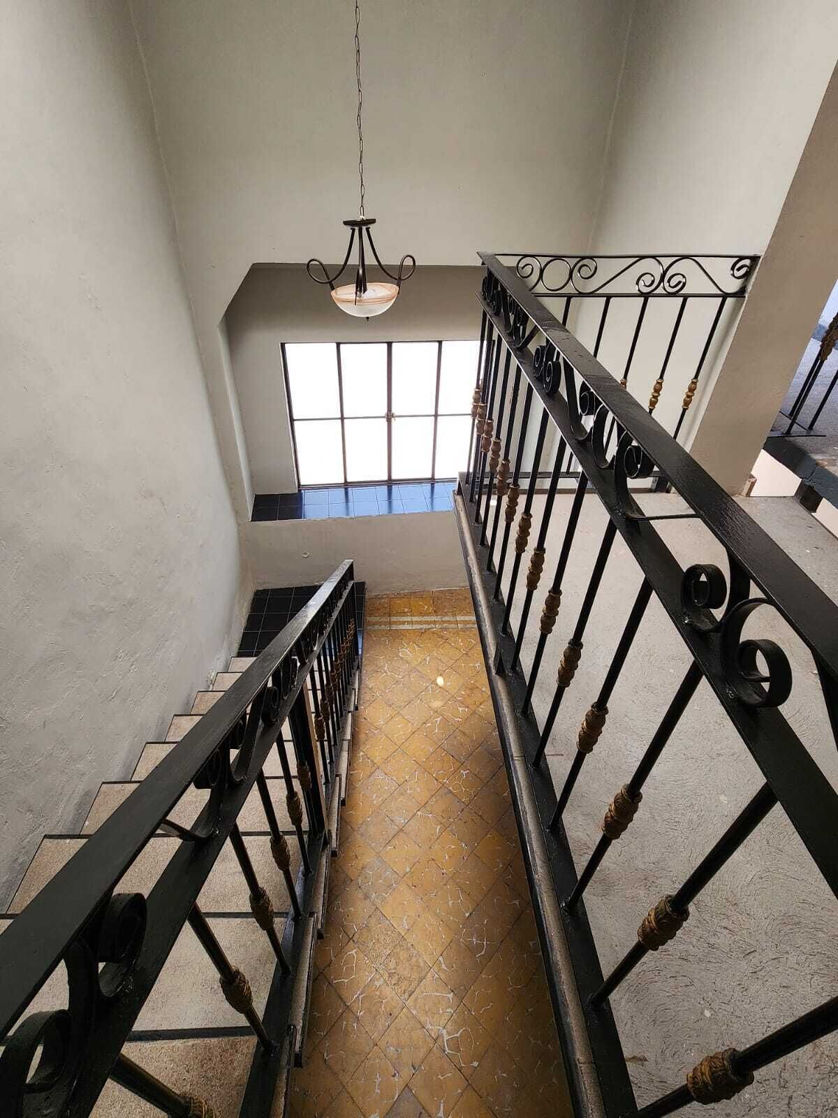 A staircase with black metal railings, a hanging light fixture, and a view of the outside through a window.