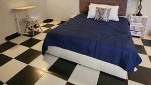 A bedroom with a checkered floor, a bed with a headboard, a nightstand, a lamp, and a chair.