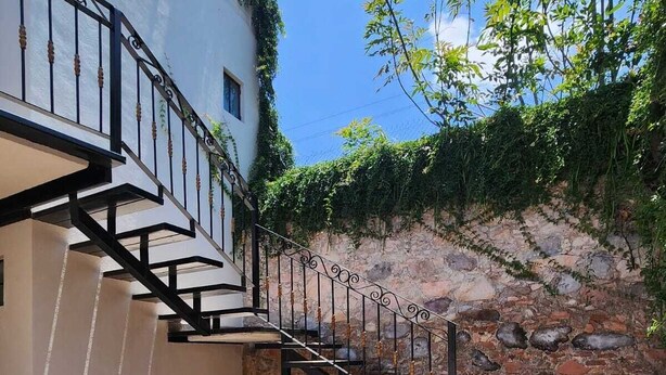 A staircase leading to a white building with a stone wall and greenery.