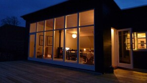 Ein modernes Gebäude mit großen Fenstern, einer Terrasse und einem sichtbaren Innenraum mit Möbeln.