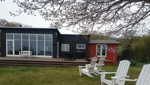 Ein modernes Haus mit Terrasse, Sitzgelegenheit im Freien und einem roten Gartenhaus.