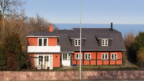 Ein zweistöckiges Haus mit einer Steinsäule im Vordergrund, freier Blick auf das Meer und einer Straßenlaterne.