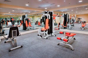 Un gimnasio con diversas máquinas de ejercicio, espejos y suelo cubierto de alfombra.