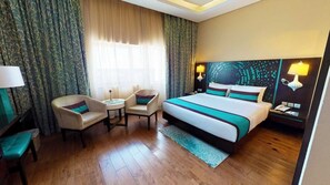 Habitación de hotel con una cama grande, dos sillones, una mesita, un escritorio y una mesita de noche con lámparas.